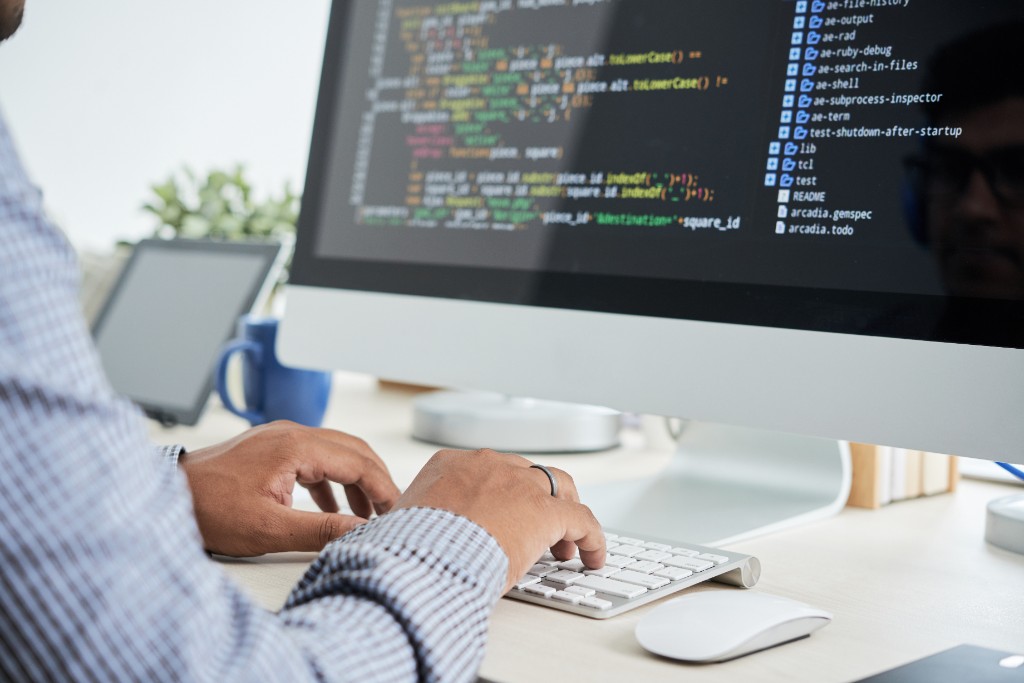 Hands typing at a keyboard beside a screen of code.